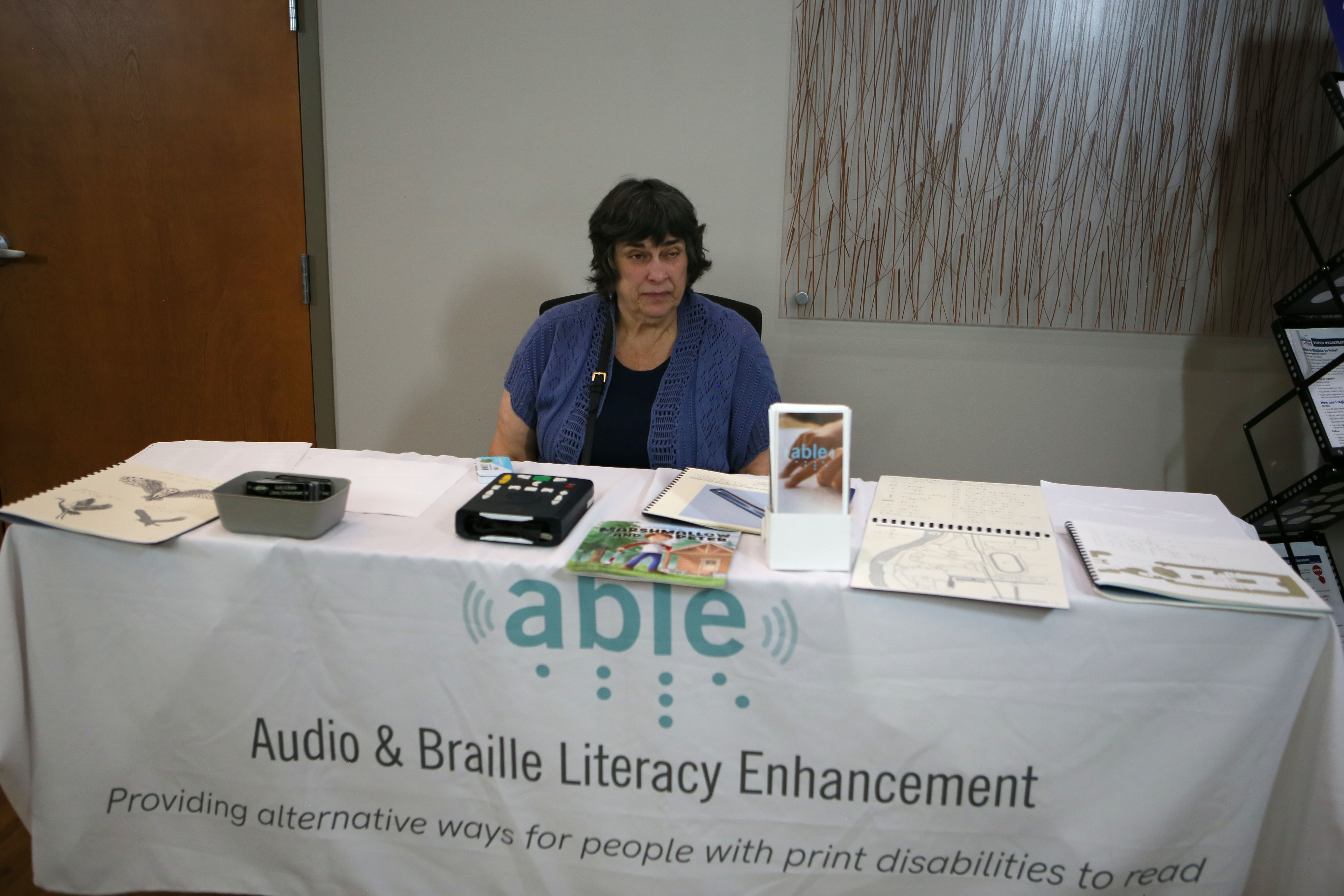Cheryl Orgas sits at the table for Audio & Braille Literacy Enhancement at the resource fair