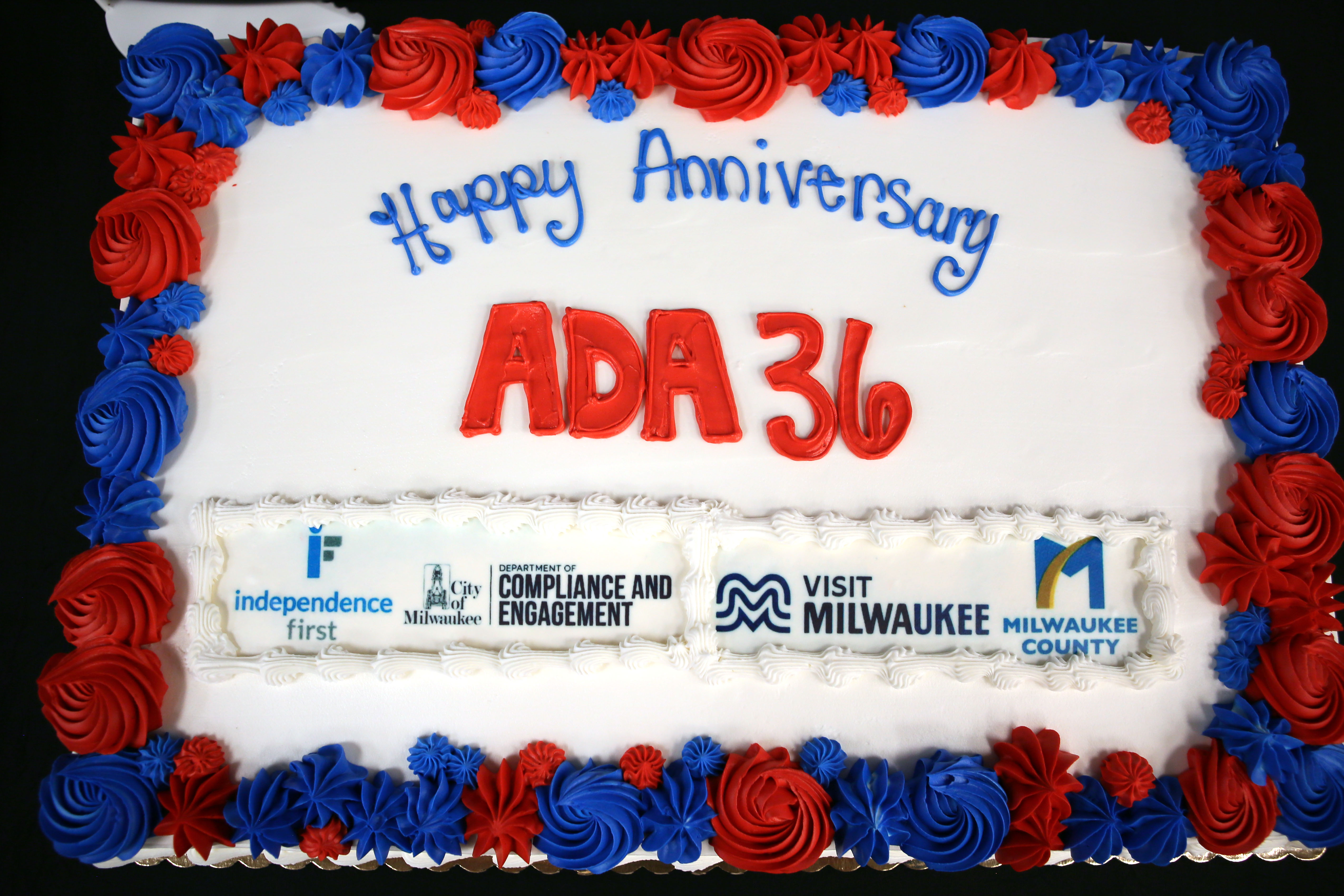 A large sheet cake celebrates the 36th anniversary of the Americans with Disabilities Act. Decorated with red, white, and blue frosting, the cake reads "Happy Anniversary ADA 36"