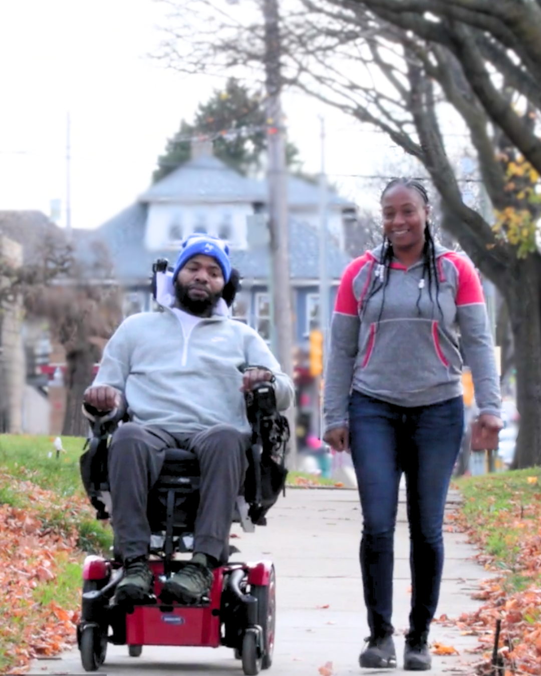 A male consumer using a wheelchair with a female personal care worker walking beside him on a city sidewalk