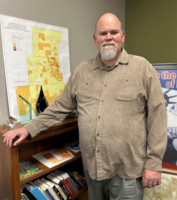 A man with a grey goatee and brown shirt poses for a photograph