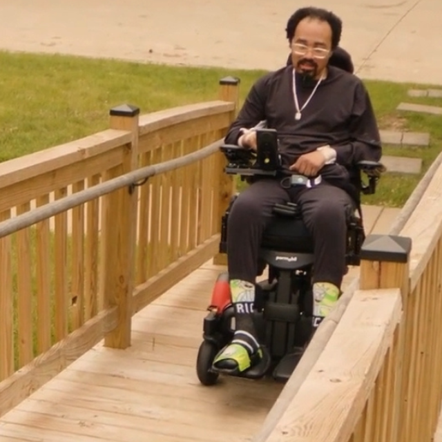 Man using a power wheelchair to move up a wooden ramp