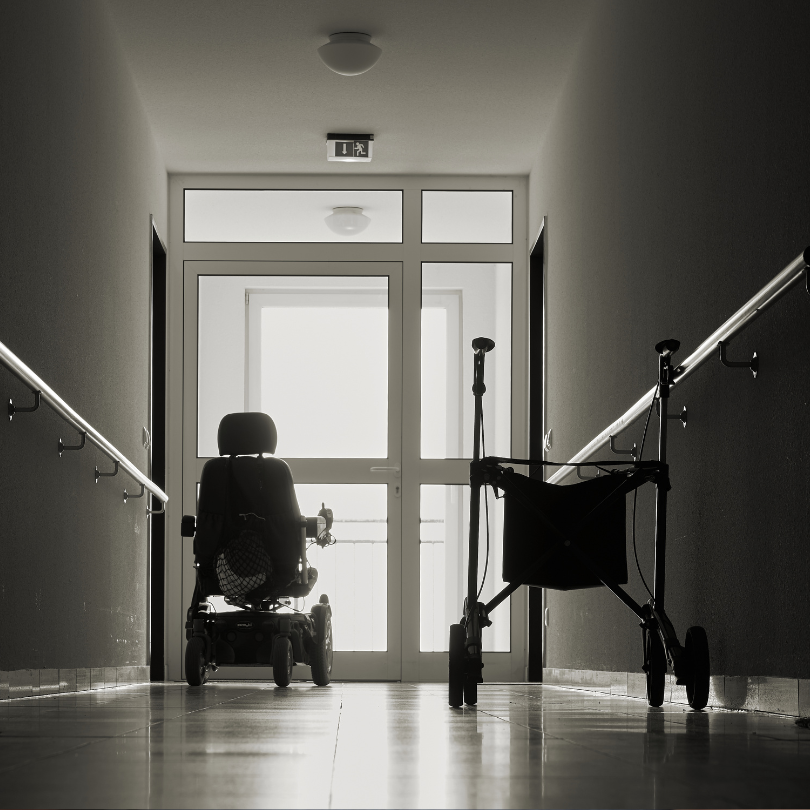 Black-and-white photograph of a dimly lit hallway with handrails along both walls. An empty powered 