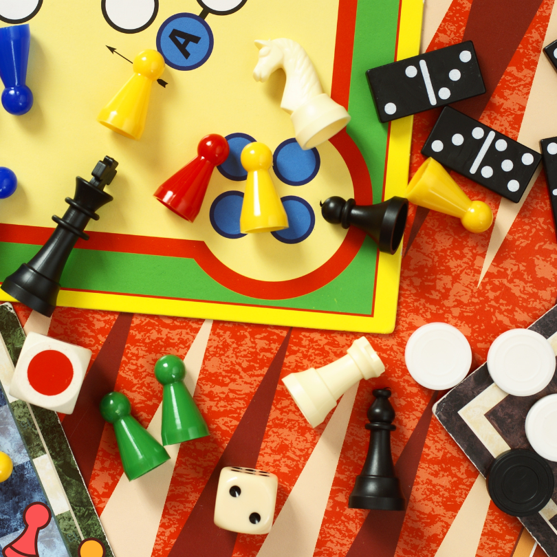 A colorful assortment of board game pieces and tabletop game components scattered across several gam