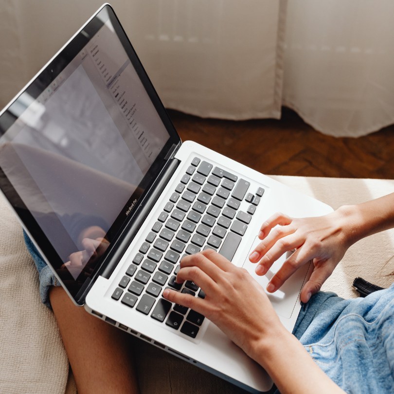 Close-up photo of a person using a laptop computer while seated indoors. Their hands are typing on t