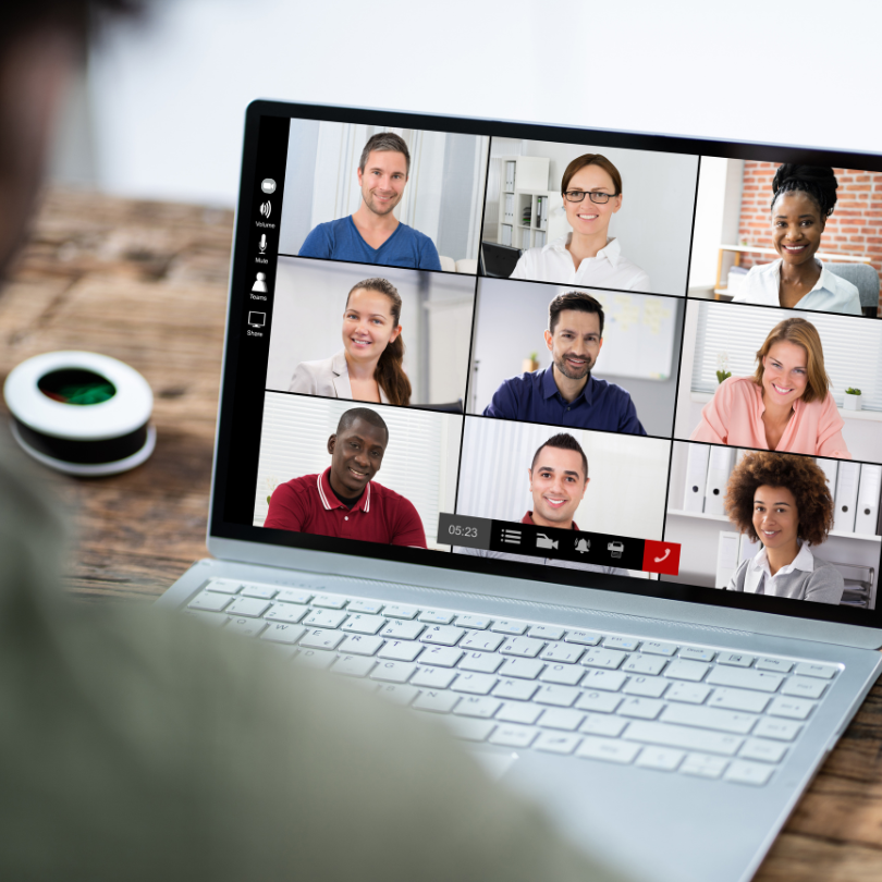 A laptop on a desk displays a virtual video meeting with nine participants arranged in a grid.