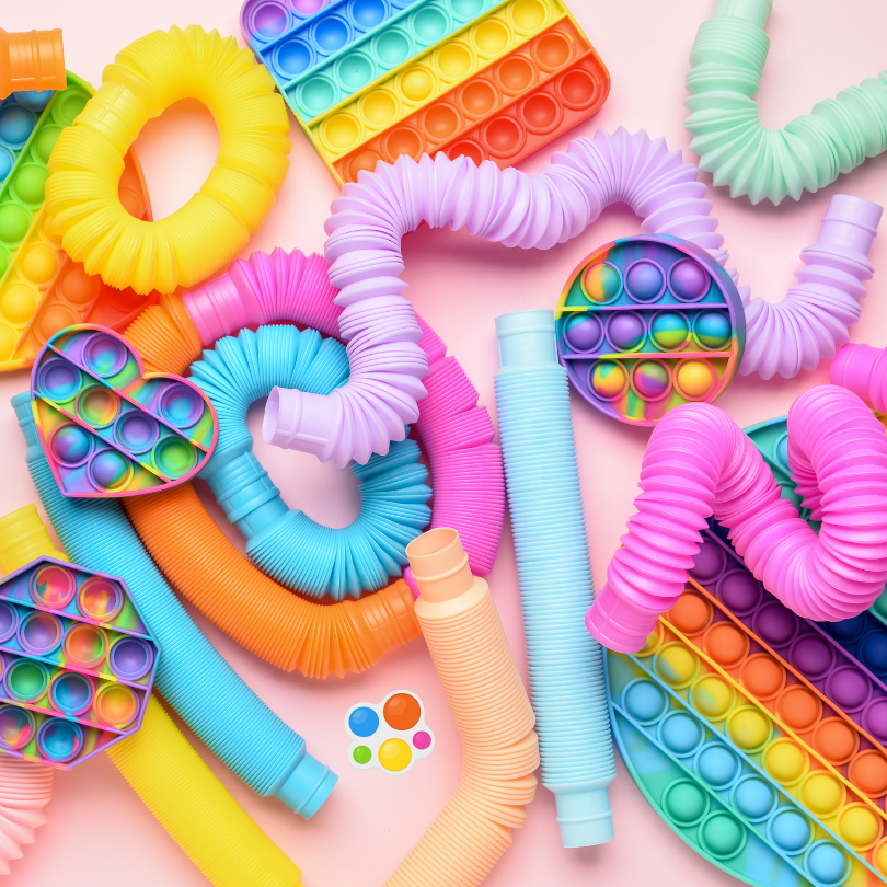 A colorful assortment of sensory fidget toys, including rainbow pop-it boards, flexible textured tub