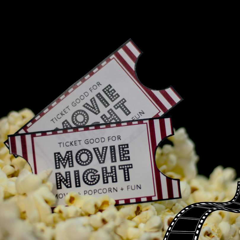 Two decorative movie night tickets resting in a pile of popcorn against a black background.