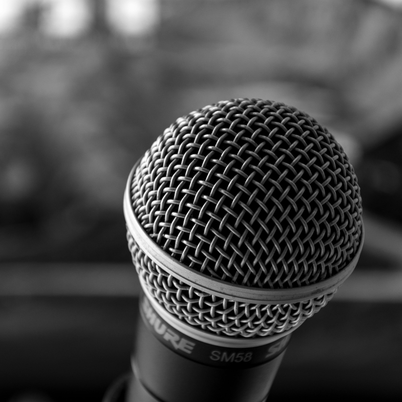 Black-and-white close-up photograph of a handheld microphone with a metal mesh grille in sharp focus