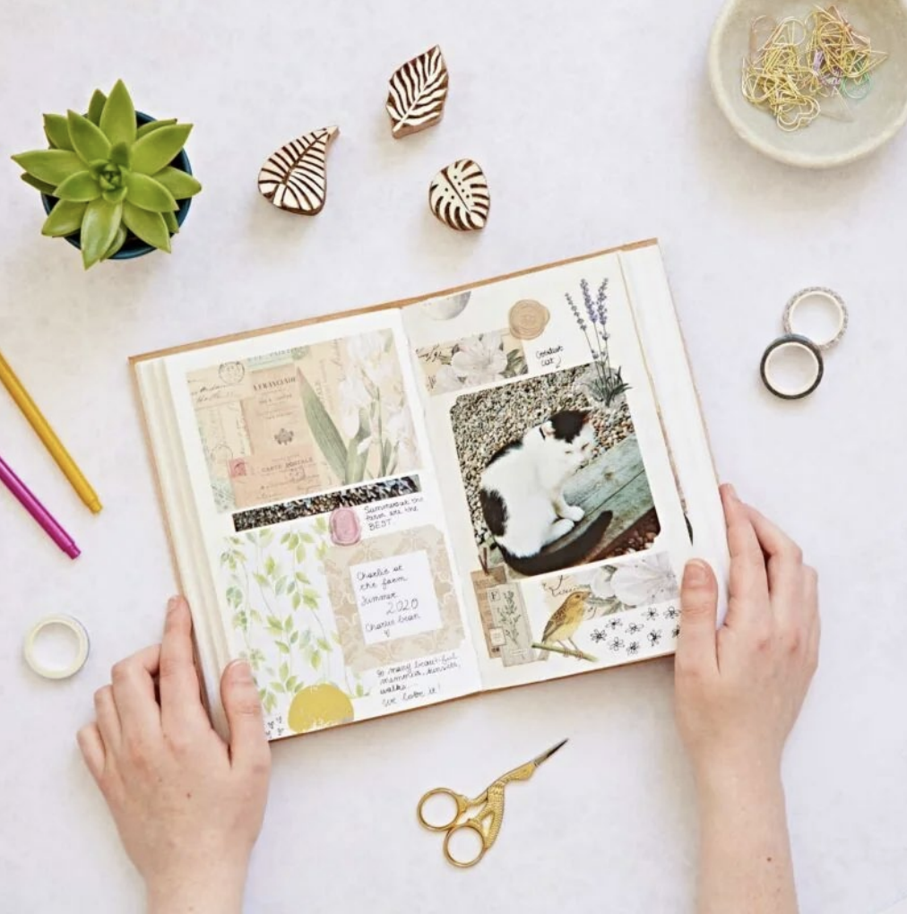 photo of hands holding a scrapbook with art supplies surrounding them on a table