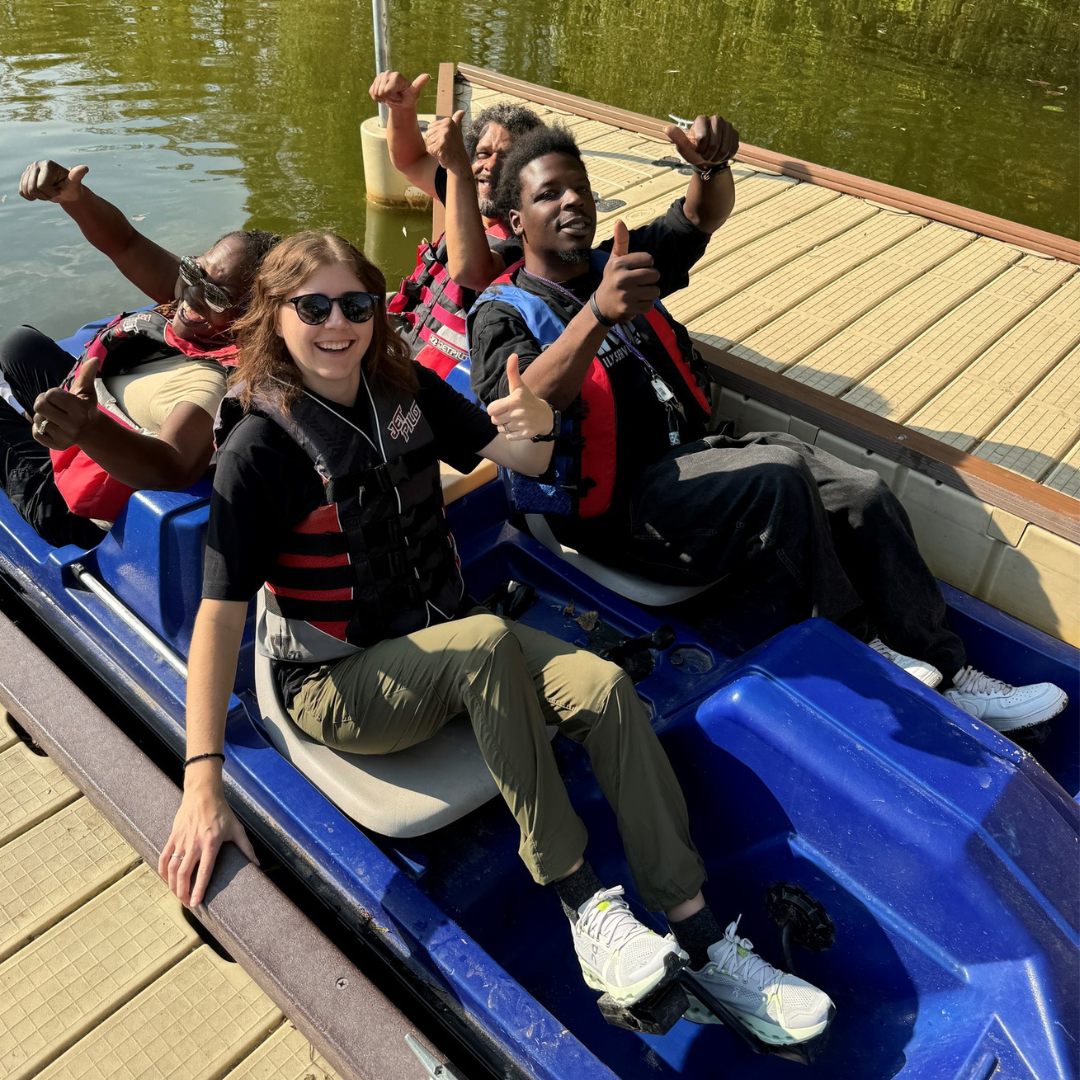 A paddleboat next to a dock filled with smiling people posing for the camera