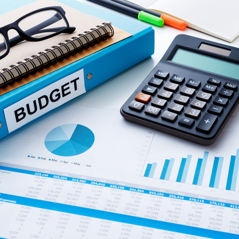A desk with a calculator, glasses, a binder that says budget and charts and graphs