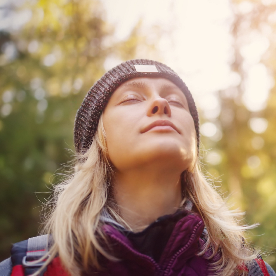 Woman's face with eyes closed, looking content with sun and woods behind her