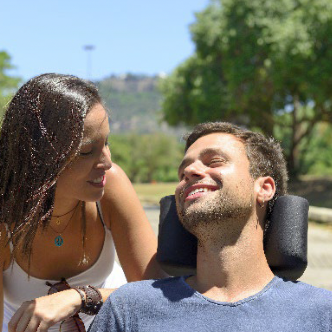 a couple smile at each other, with one person seated in a wheelchair