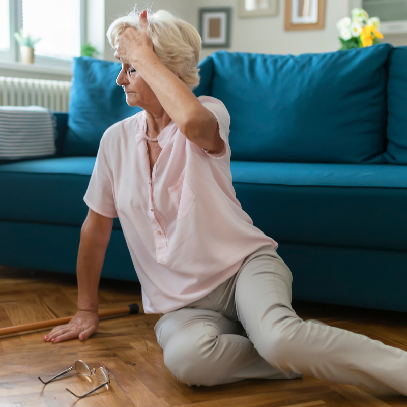 A woman on the ground grabbing her head with glasses and a cane fallen beside her