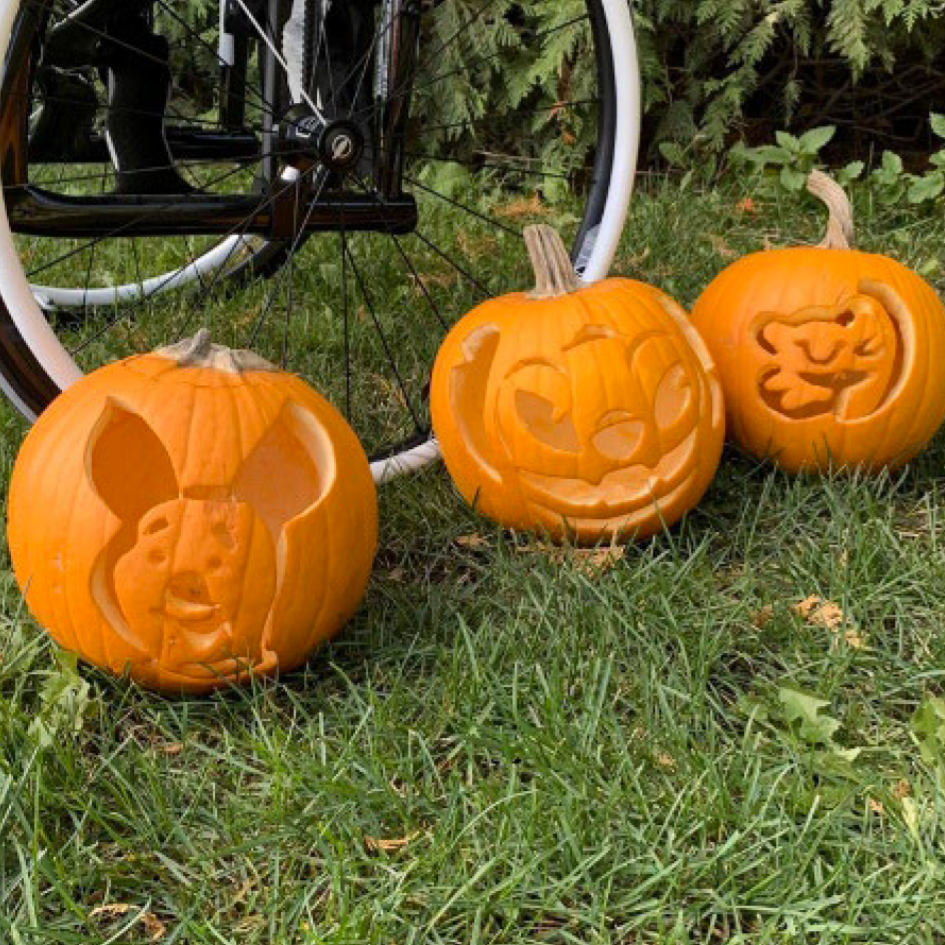 Carved pumpkins in grass next to a wheelchair wheel