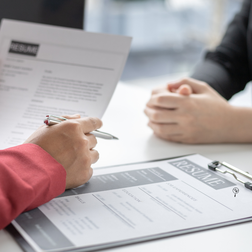 Close-up of two people sitting across from each other reviewing a resume during a job interview, wit