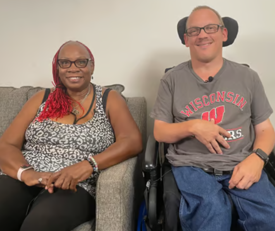 Photo of caregiver Denise sitting on a couch next to consumer Mike seated in a wheelchair
