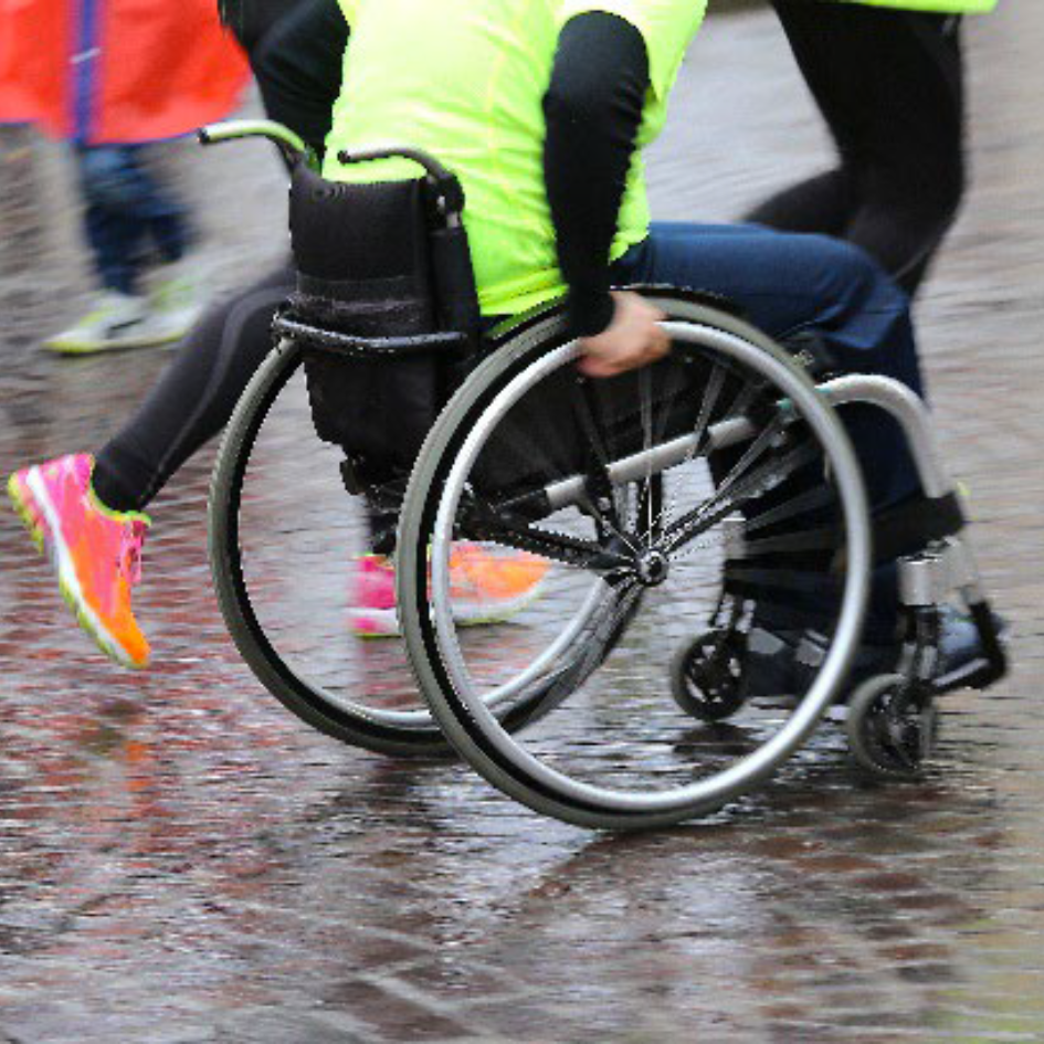 A person in a wheelchair and two runners participate in a race in the rain