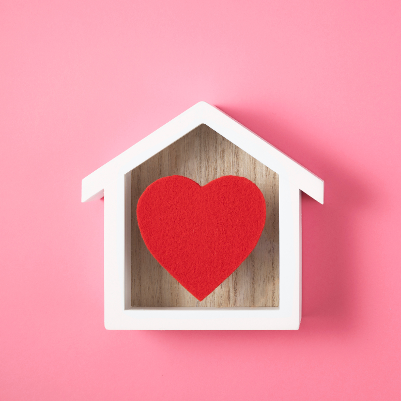 A white house-shaped frame sits against a pink background, with a red heart centered inside on a woo