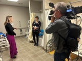 A reporter interviews an Independence First staff member inside the Bathroom Assistive Technology room.