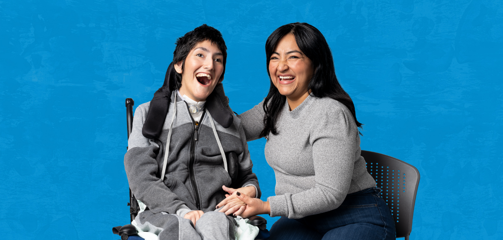 Two smiling people, one in a powerchair and one in an office chair