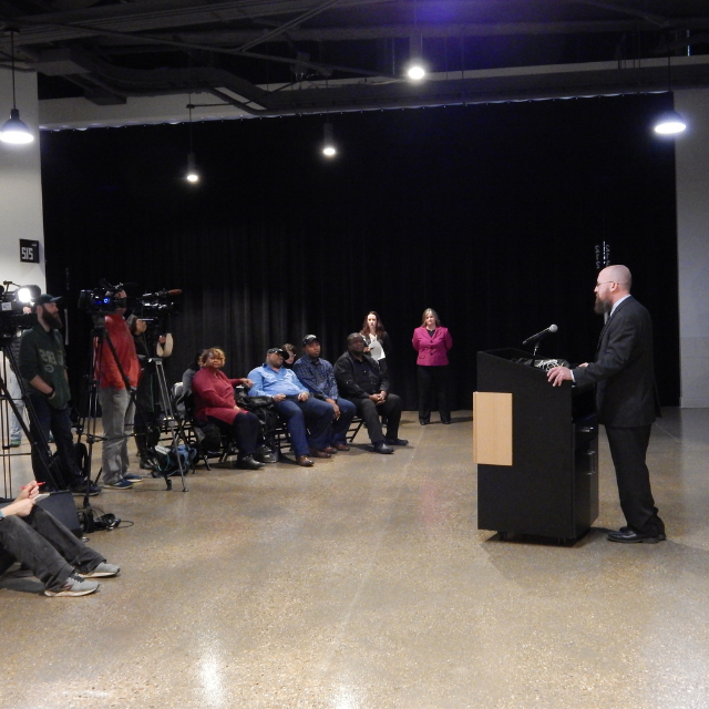 A man is standing a podium speaking to an audience.