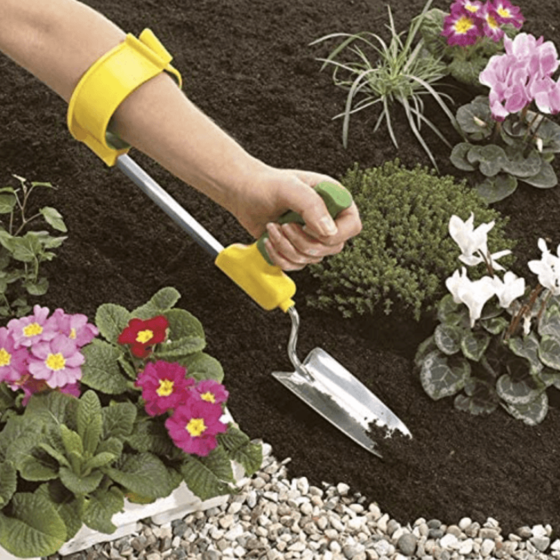 A woman's arm and hand seen using an adaptive gardening tool to dig in soil.