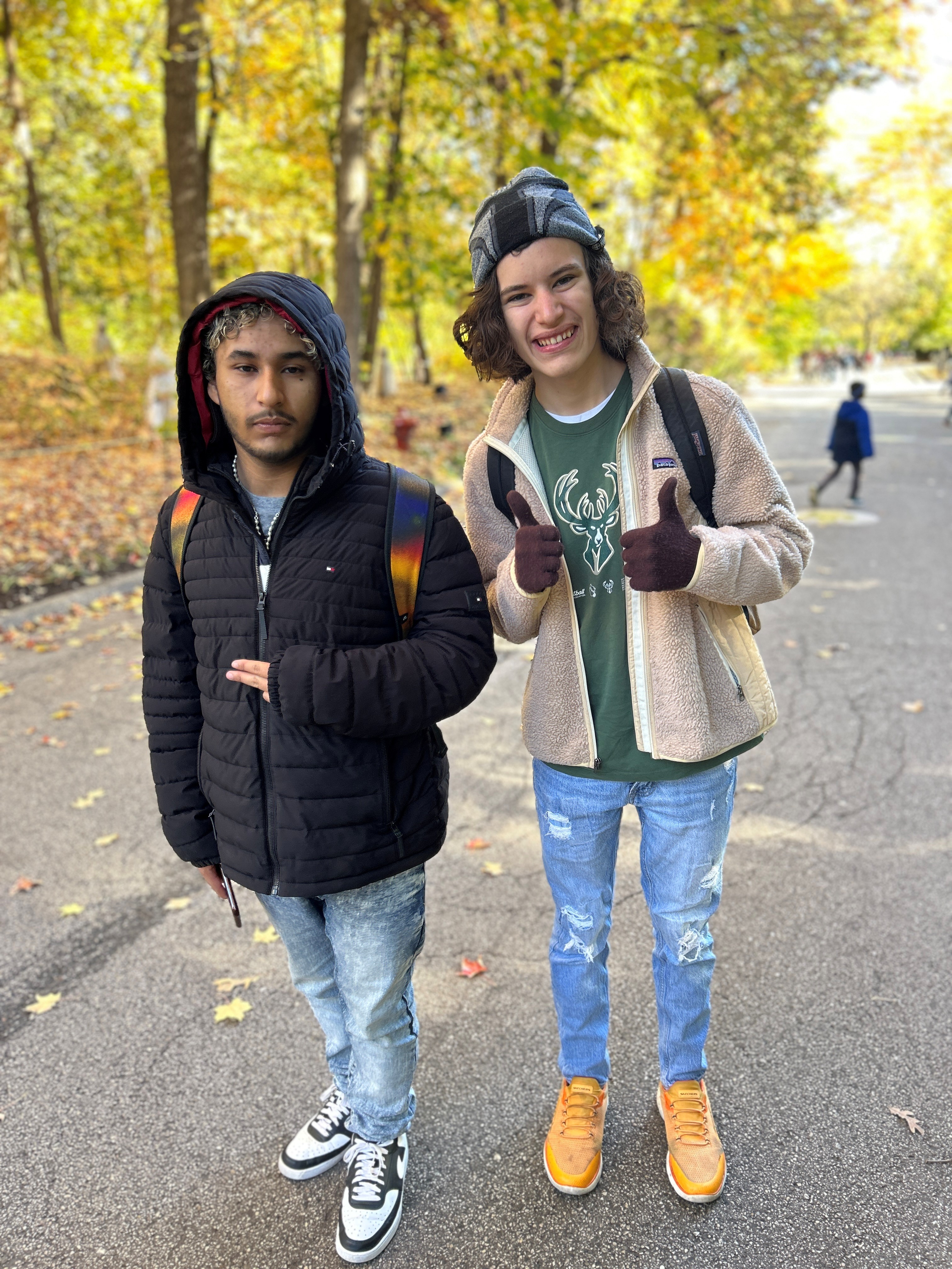 Two teens pose for a photo smiling. The young man on the right shows two thumbs up.