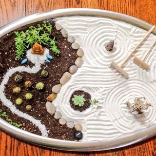 Zen garden with plants, stones, dirt and white sand with rakes creating calming patterns