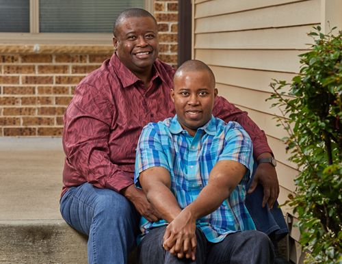 two African American men sitting on steps in front of a house