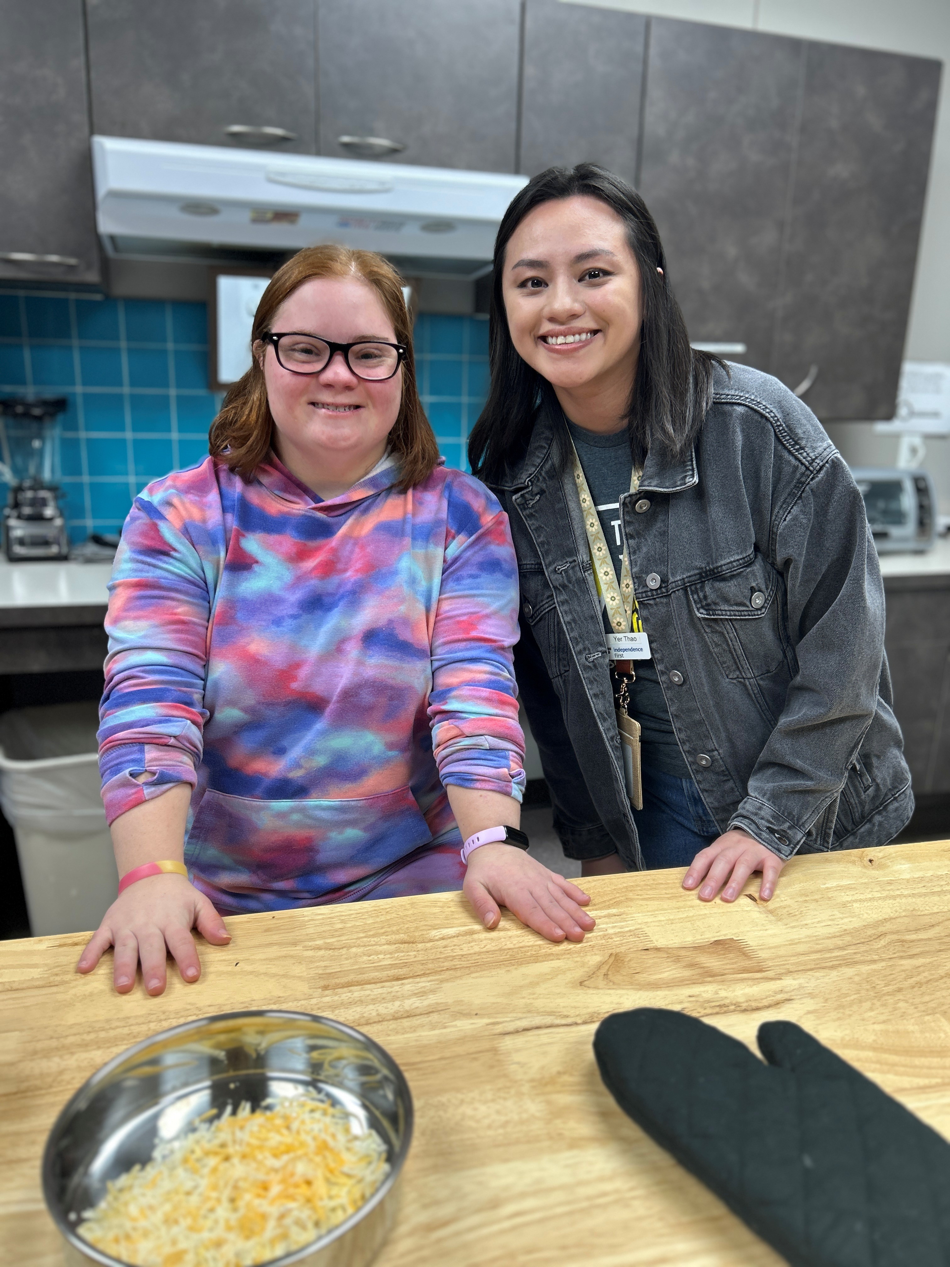 Two young women pose for a photo smiling in a kitchen.