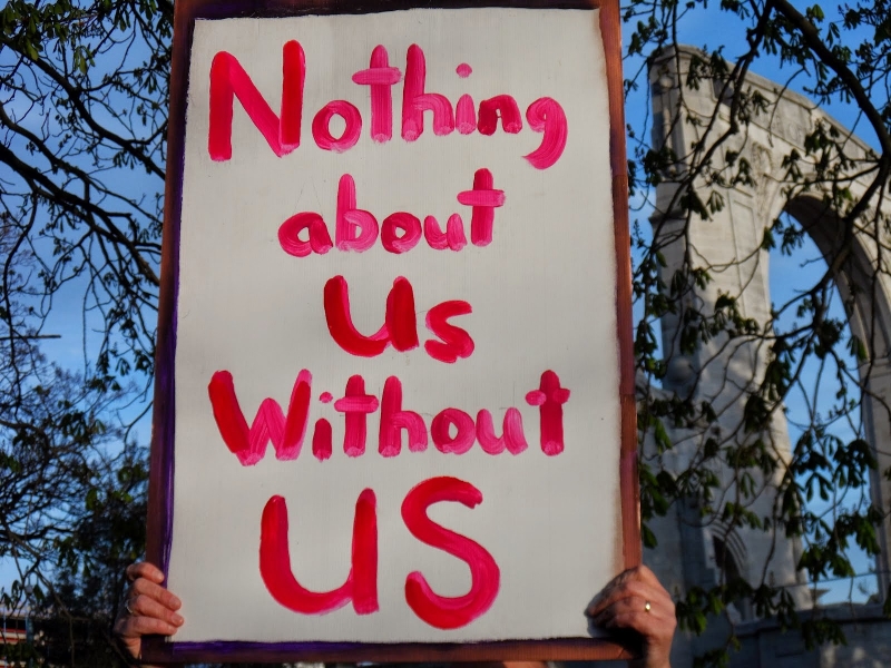 Poster sign that reads "Nothing About Us Without Us" in red lettering